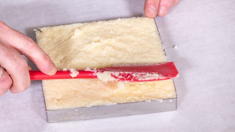 Der Konditor streicht den Teig für die süßen Grießschnitten in einer Form glatt. 