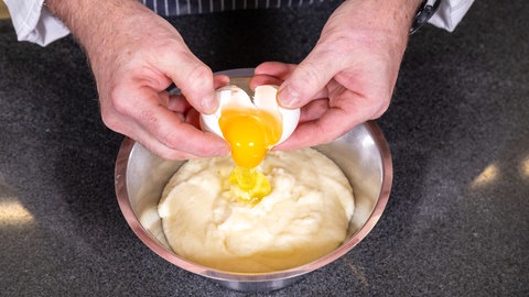 Der Konditor gibt Eier in den Topf mit Teig hinzu. 