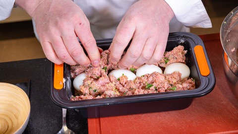 Eine Kastenform gefüllt mit einer Hackfleischmasse und gekochten Eiern. Daraus wird "Falscher Hase" gemacht.