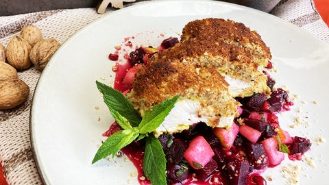 Rezept Hähnchenbrust mit Nusskruste: Stück Hähnchenbrust mit Nusskruste auf rote Bete Salat mit einem Strauß Minze auf einem weißen Teller