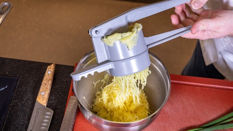 Eine gelbe Masse wird mit zwei Händen durch eine Presse in eine Schale gedrückt