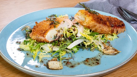 Spargel umwickelt mit Schinken und Käse und lecker paniert liegt auf einem Salatbett auf einem Teller.