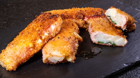 Panierte Spargelröllchen liegen auf einer Platte und sind aufgeschnitten, damit man die Schinken-Käse-Füllung sehen kann.