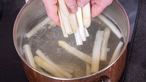 Frischer Spargel wird zum Kochen in einen Topf mit Salzwasser gegeben.