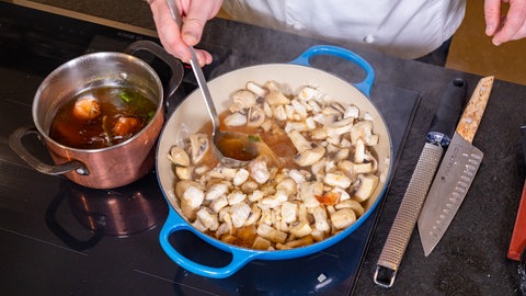 Rezept Ragout fin: Pilze in einer Pfanne werden mit einer Brühe abgelöscht.