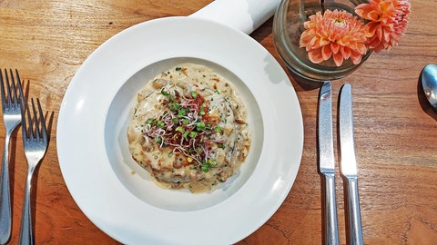 weißer Teller mit Waldpilzragout auf Holztisch, daneben Besteck und eine Blume