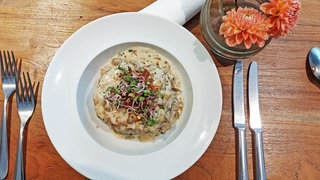 weißer Teller mit Waldpilzragout auf Holztisch, daneben Besteck und eine Blume