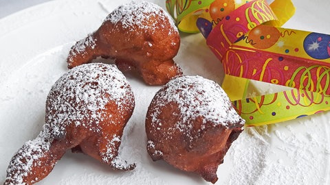 weißer Teller mit braunen Gebäckkugeln (rheinische Mutzen) mit Luftschlangen daneben