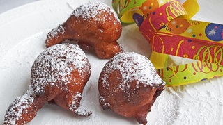 weißer Teller mit braunen Gebäckkugeln (rheinische Mutzen) mit Luftschlangen daneben