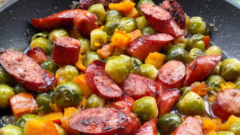 Rezept: Rosenkohl, Karotten und Mettenden angebraten in einer Pfanne.