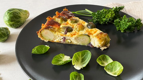 schwarzer Teller mit einem Stück Rosenkohl-Quiche, drumherum Rosenkohlblätter