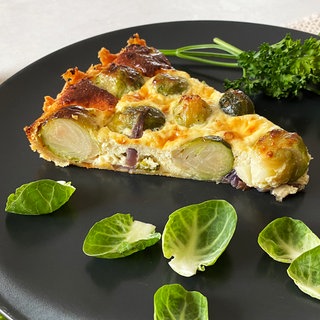 schwarzer Teller mit einem Stück Rosenkohl-Quiche, drumherum Rosenkohlblätter