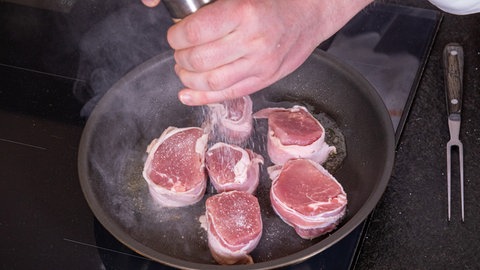 Schweinemedaillons im Speckmantel in fruchtiger Soße: Die Medaillons in der Pfanne werden gesalzen.