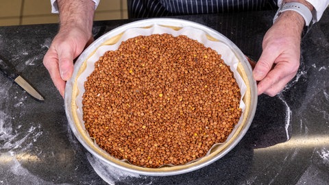 Die Backform mit dem Teig ist mit Backpapier ausgelegt, und mit Linsen befüllt. 