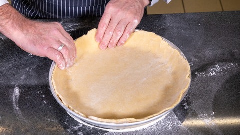 Der Koch knetet den Teig in die runde Backform. 