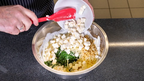 Der Koch gibt Käsewürfel in die Schüssel hinzu. 