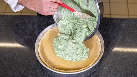 Der Koch kippt die Füllung in die mit Teig ausgelegte Backform. 