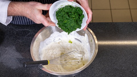 Der Koch gibt in eine Schüssel mit Schmand den Spinat dazu. 