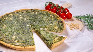 Rezept Spinat-Feta-Quiche: Eine fertig gebackene Quiche mit Belag aus Spinat und Feta, ein Stück herausgeschnitten.