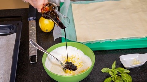Aus Schmand, Knoblauch, Sojasoße, Salz, Pfeffer und Zitronenabrieb wird eine cremige Masse für eine Tomaten-Tarte hergestellt.