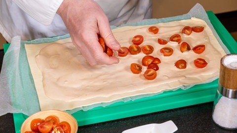 Der Blätterteig für eine Tomaten-Tarte wird mit kleingeschnittenen Kirschtomaten belegt.