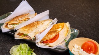 Rezept für Tortilla-Sandwich: Die frisch angerichteten Tortilla-Sandwiches, eingepackt in Brotpapier und verzehrfertig als Fingerfood.
