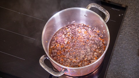Mit Rotwein werden das Pancetta, die Karotten, Sellerie und Zwiebelstückchen in einem Topf zu einer original italienischen Bolognese alla Ragu gekocht.