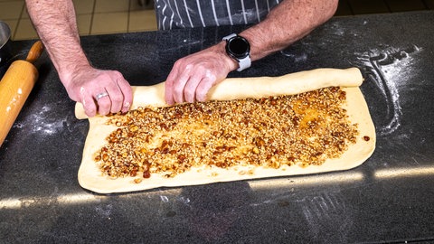 Der mit Nussfüllung bestrichene Zimtschnecken-Hefeteig wird aufgerollt.