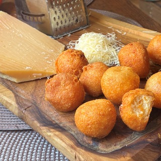 Goldgelbe Käsebällchen liegen auf einem Holzbrett, zusammen mit geriebenem Käse und einer Käsereibe. SWR1 Pfännle Rezept für goldgelbe Käsebällchen mit nur zwei Zutaten: Das ist ein schneller, knuspriger und unkomplizierter Snack oder eine leckere Beilage.