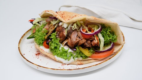 Auf einem Teller liegt ein Pfannendöner mit Fleisch, Grillgemüse, Salat und Sauce in einem Dönerbrot. Es gibt verschiedene Möglichkeiten ihn selber zuhause zu machen, SWR1 Pfännle-Koch Eberhard Braun zeigt euch die Pfannendöner-Variante.