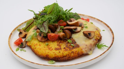 Schweizer Rösti mit Salatblättern, Tomaten und Pilzen angerichtet auf einem Teller.