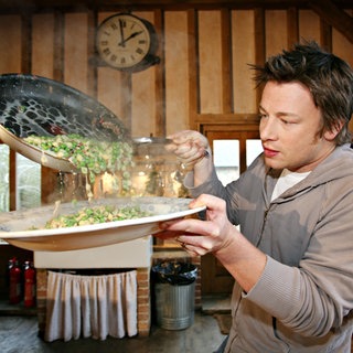 Jamie Oliver kippt Essen aus einer Pfanne in einen Teller