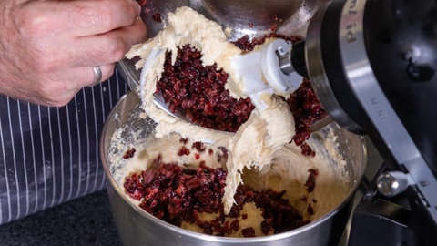 Die im Rezept vorgegebene Menge an Cranberrys wird aus einer Schüssel zur Teigmasse für den Stollen in einer Teigrührmaschine hinzugefügt.