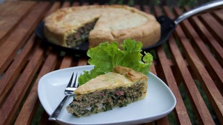 Ein Stück einer Maultaschen-Quiche steht auf einem Teller auf dem Tisch.