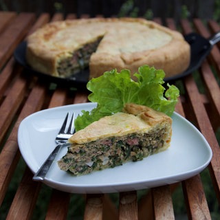 Ein Stück einer Maultaschen-Quiche steht auf einem Teller auf dem Tisch.