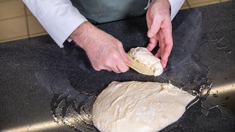Teig wird auf einer feuchten Oberfläche zu länglichen Brötchen geformt