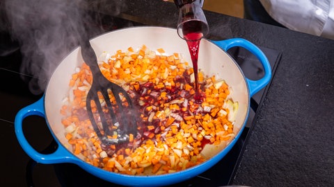 Die angeschwitzten Karotten- und Zwiebelwürfel sowie der Knoblauch werden für die der vegetarische Bolognese in der Pfanne mit Rotwein abgelöscht.