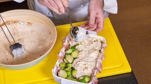 Rosenkohl und Speck werden in eine Auflaufform gegeben und mit einer cremigen Masse übergossen.