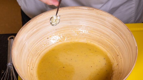 Ein Koch gibt gehackten Knoblauch in eine Schüssel mit einem Dressing für einen Nizza-Salat.