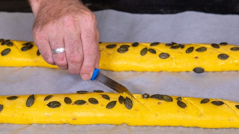 Wie im Rezept beschrieben, werden mit einem Messer die Baguette eingeschnitten. Dann mit Wasser bestreichen und mit Kürbnis-Kernen bestreuen. Die tolle Farbe hat da Baguette durch den Hokkaido.
