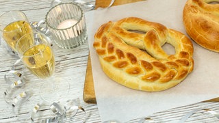 Neujahrsbrezel mit Rezept: Backen fürs neue Jahr. Zwei Brezeln sind neben gefüllten Sektgläsern angerichtet.