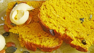 zwei Scheiben gelbliches Kürbisbrot mit einem Stück gerollte Butter auf einem grünen Teller