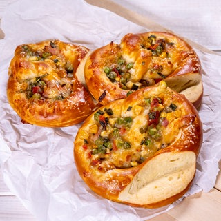 Drei fertig gebackene mit Gemüse und Schinken gefüllte Brezeln liegen im Dreieck ein wenig übereinander auf einem Holzbrett