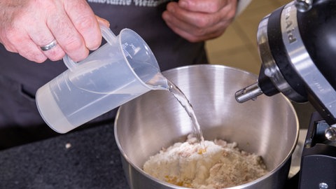 Zubereitung des Tomatenbrots: Wasser wird zu den restlichen Zutaten in die Rührschüssel gegeben.