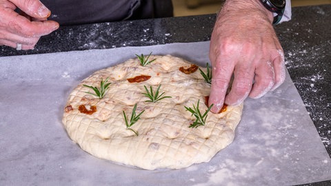 Zubereitung Tomatenbrot: Der Brotteig wird mit Tomaten und Rosmarin dekoriert.