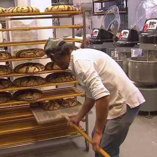 Ein Bäcker legt Brotlaibe in ein Regal