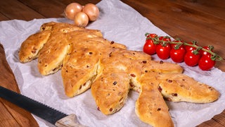 Brot aus Dinkel mit Speck und Zwiebeln: Das knusprig gebackene Brot liegt mit Cocktailtomaten garniert bereit.