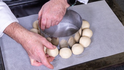 Teigkugeln für den gefüllten Laugenkranz auf einem Backblech. Sie werden, wie im Rezept beschrieben, mithilfe eines Tortenrings auf das Blech gesetzt.