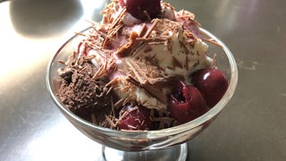 Eisbecher mit Schokoeis, Sauerkirschen, Schokoladenflakes und Sahne