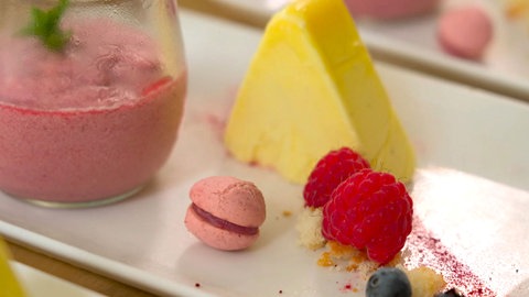 Himbeermousse mit Vanilleparfait, Sesamchip, Himbeermacarons und Himbeerspiegel auf einem Teller